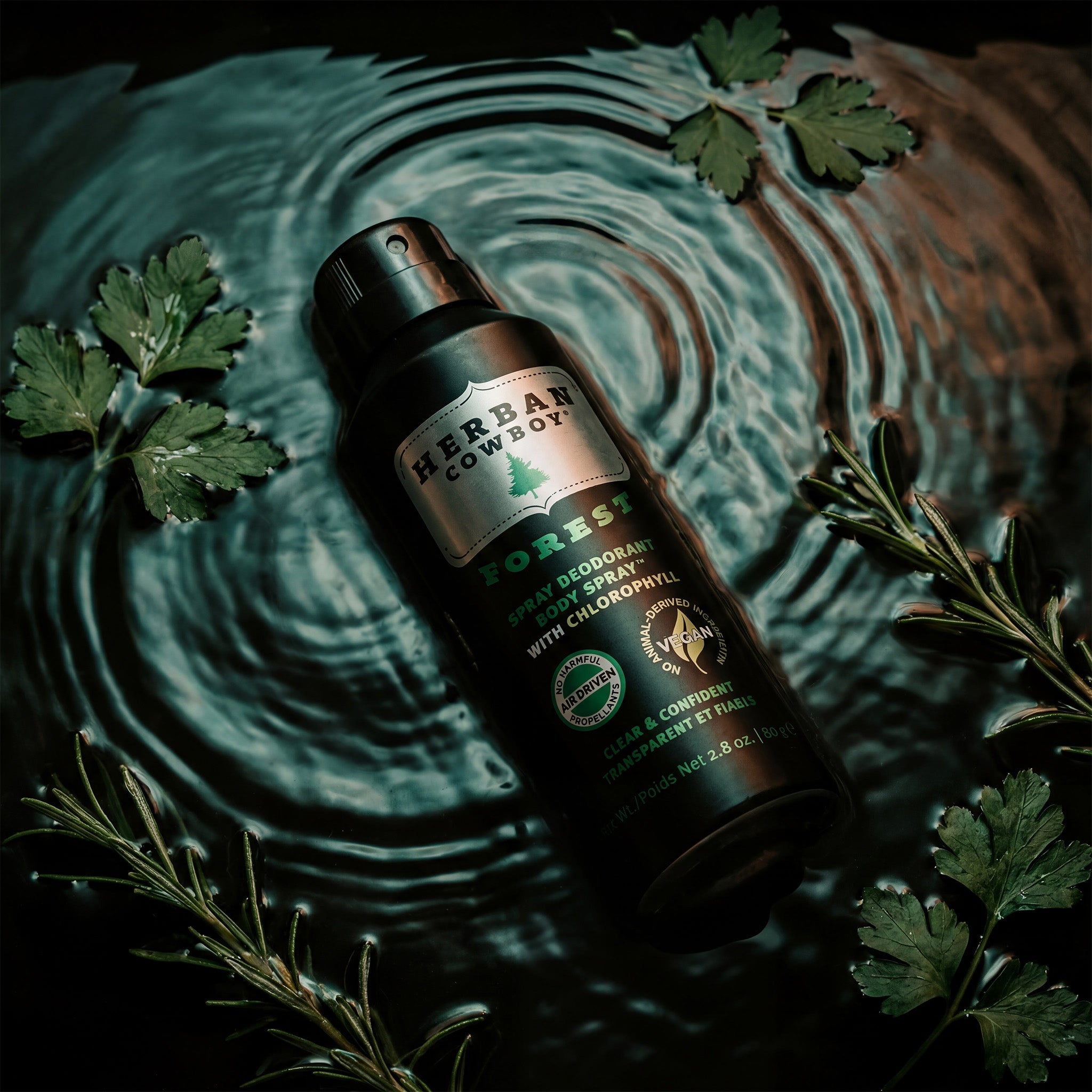 Herban Cowboy Forest deodorant spray bottle surrounded by green leaves