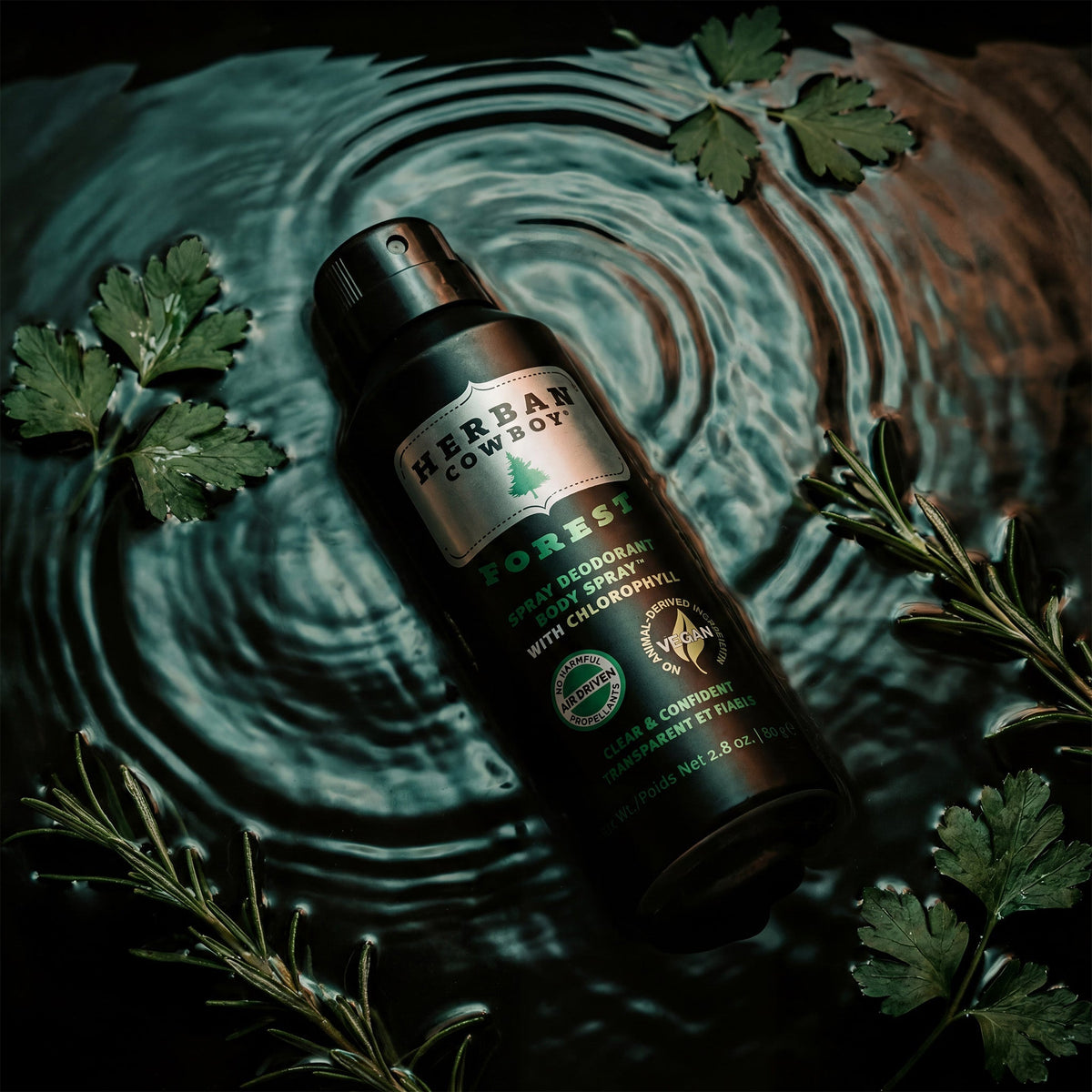 Herban Cowboy Forest deodorant spray bottle surrounded by green leaves