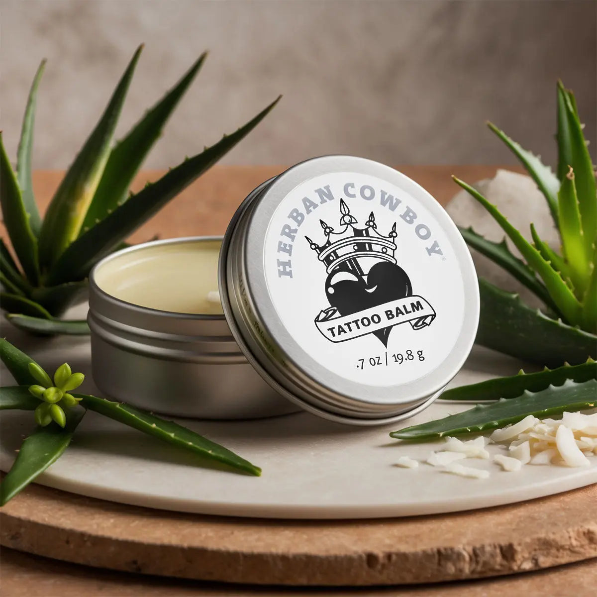 Herban Cowboy tattoo balm with aloe vera leaves on a wooden surface